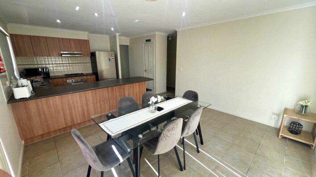Open-plan kitchen and dining area with a wooden island, stainless steel appliances, and a glass dining table with six gray chairs.