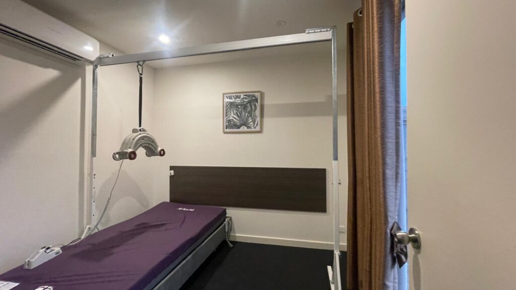Rehabilitation bed setup in a small room with a ceiling-mounted traction device and purple mattress.