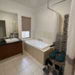 Bathroom with a white bathtub, sink vanity, and large mirror; a wheeled bath chair with teal cushions is beside a striped shower curtain.