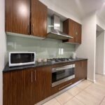 Modern kitchen with wood grain cabinets, stainless range hood, gas cooktop, built-in oven, and microwave on a dark countertop.
