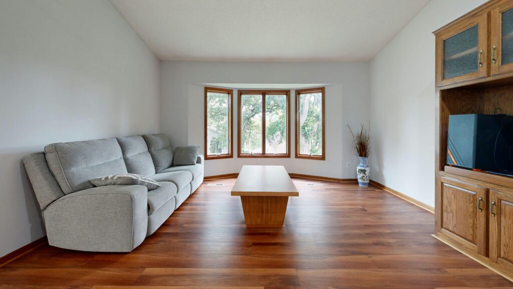 Living room with a gray sectional sofa along the left wall, a bay window in the center, a wooden coffee table, and a TV cabinet on the right.
